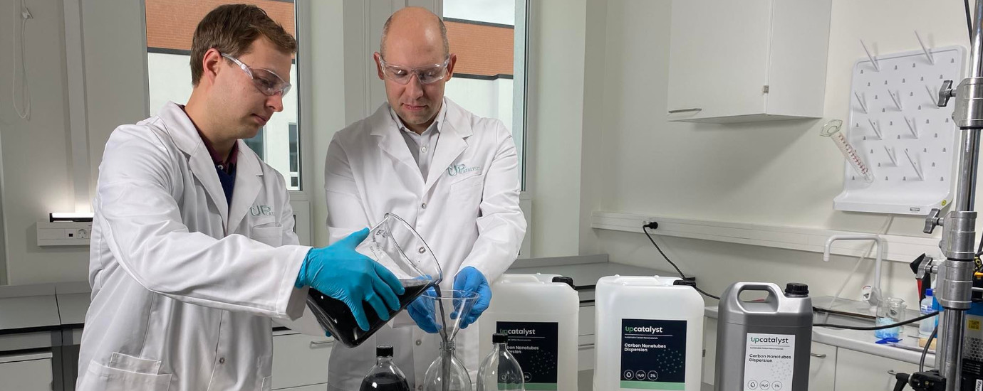 two men a laboratory pouring a black liquid in a bottle.