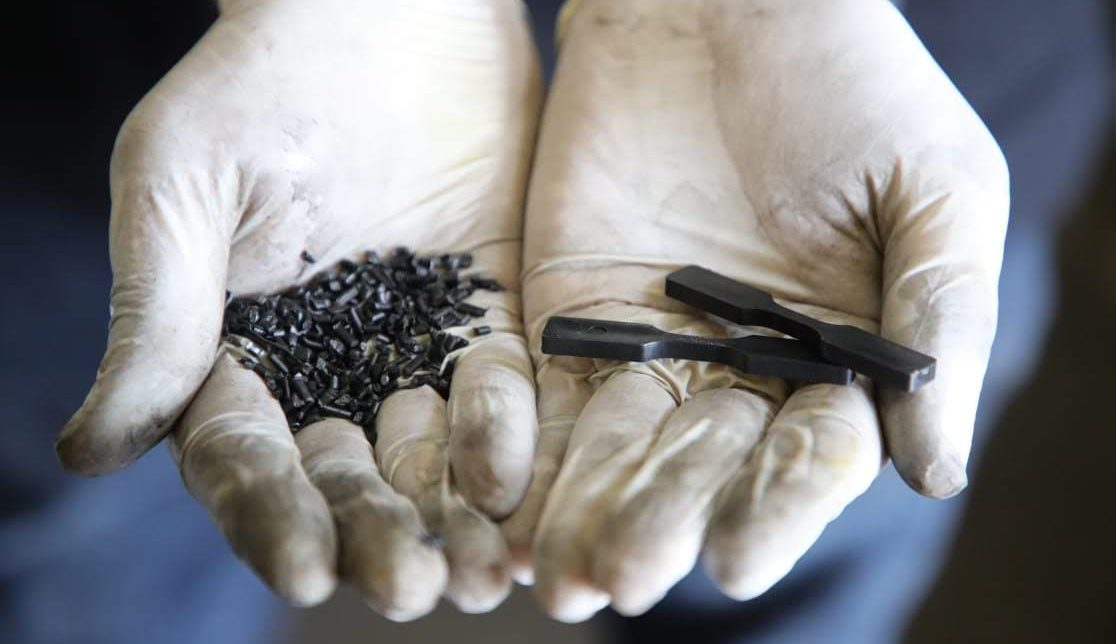 Two hands with gloves holding recycled pellets and dumbells