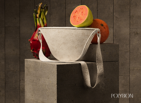 A small white bag made from a leathery material standing on a podest surrounded by fruit: dragonfruit, an orange and a cut-open papaya